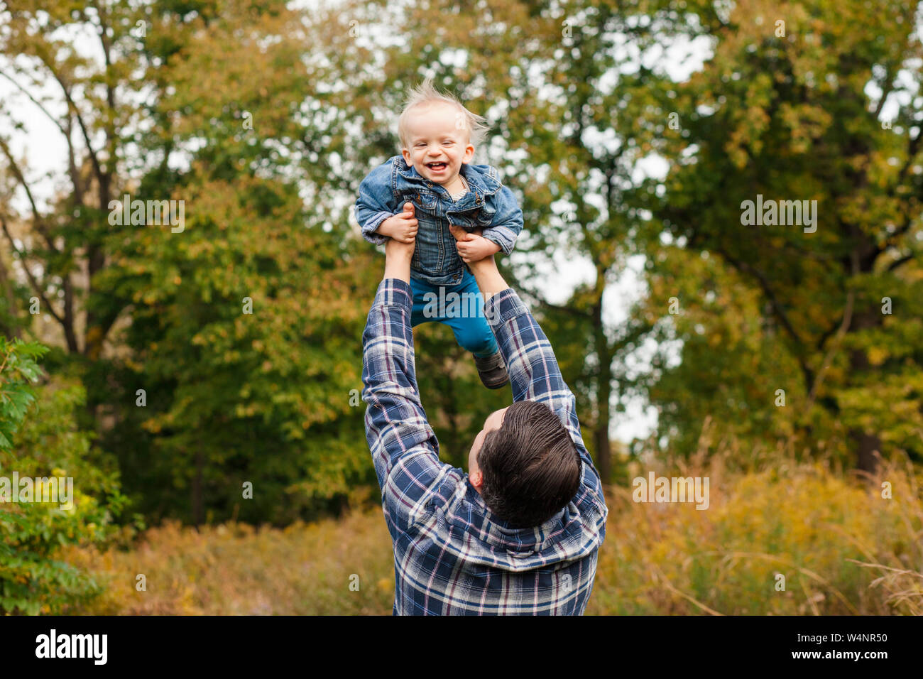 A father lifts his laughing baby boy  high up into the air outside Stock Photo