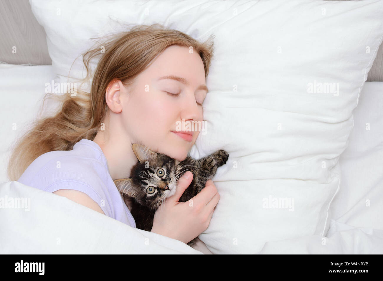 Caucasian girl with a small kitten sleeping on a white pillow in bed ...