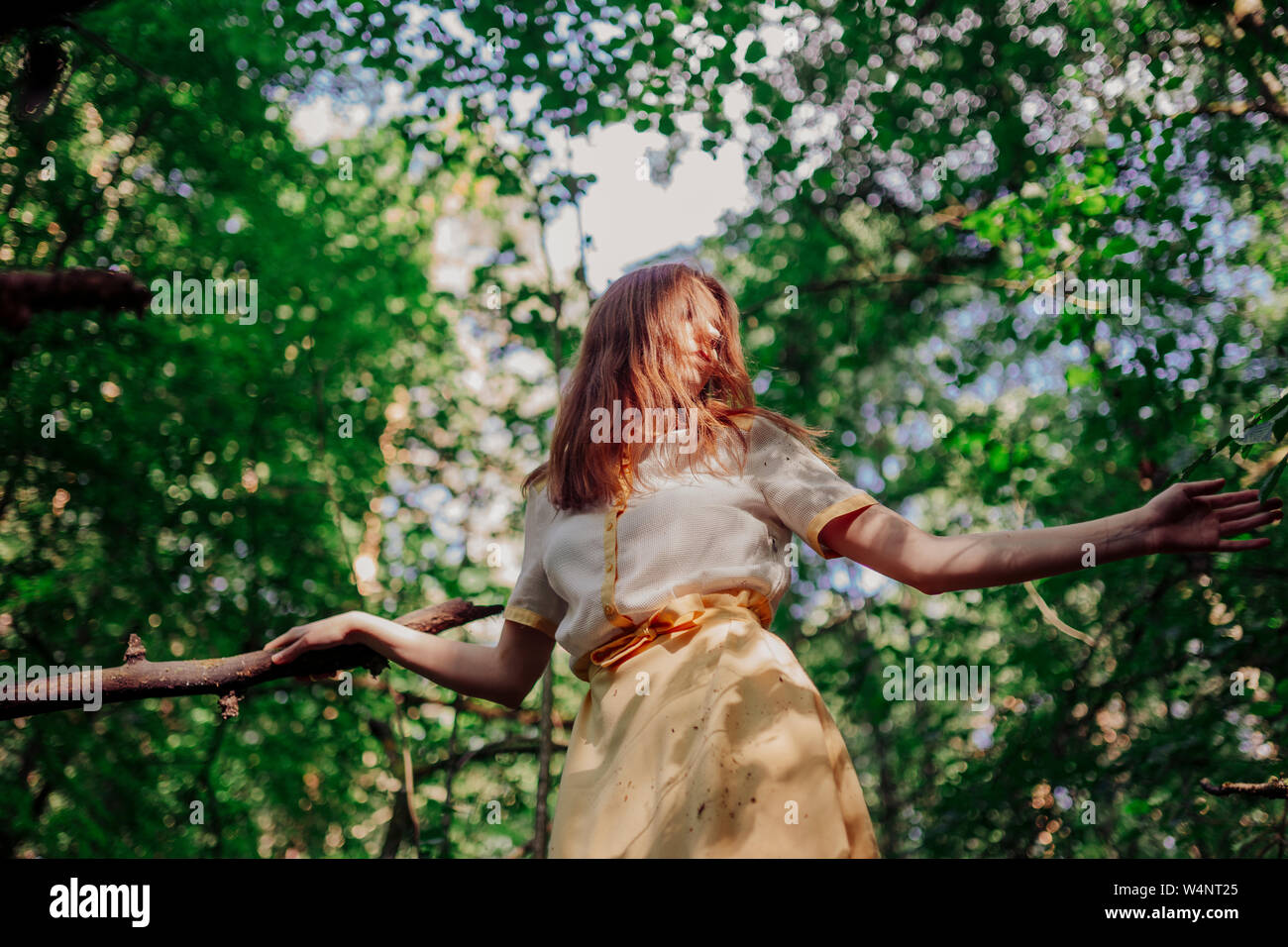 woman standing on a tree in a yellow dress Stock Photo