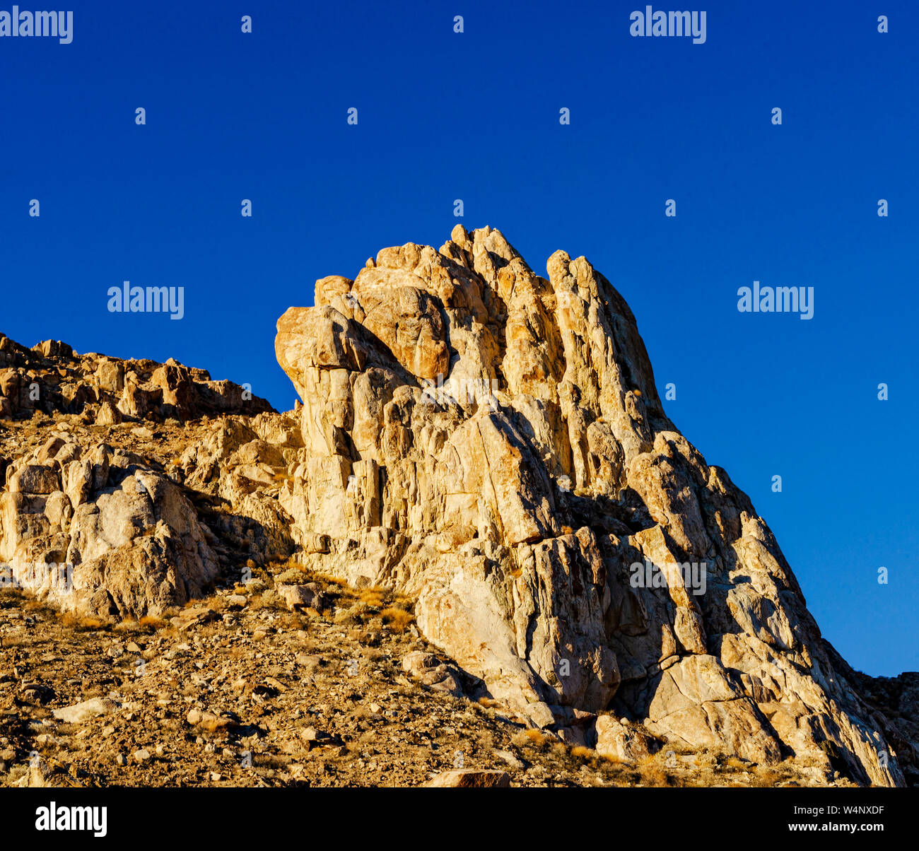 Jagged rock formation forms part of desert hillside under a bright blue sky. Stock Photo