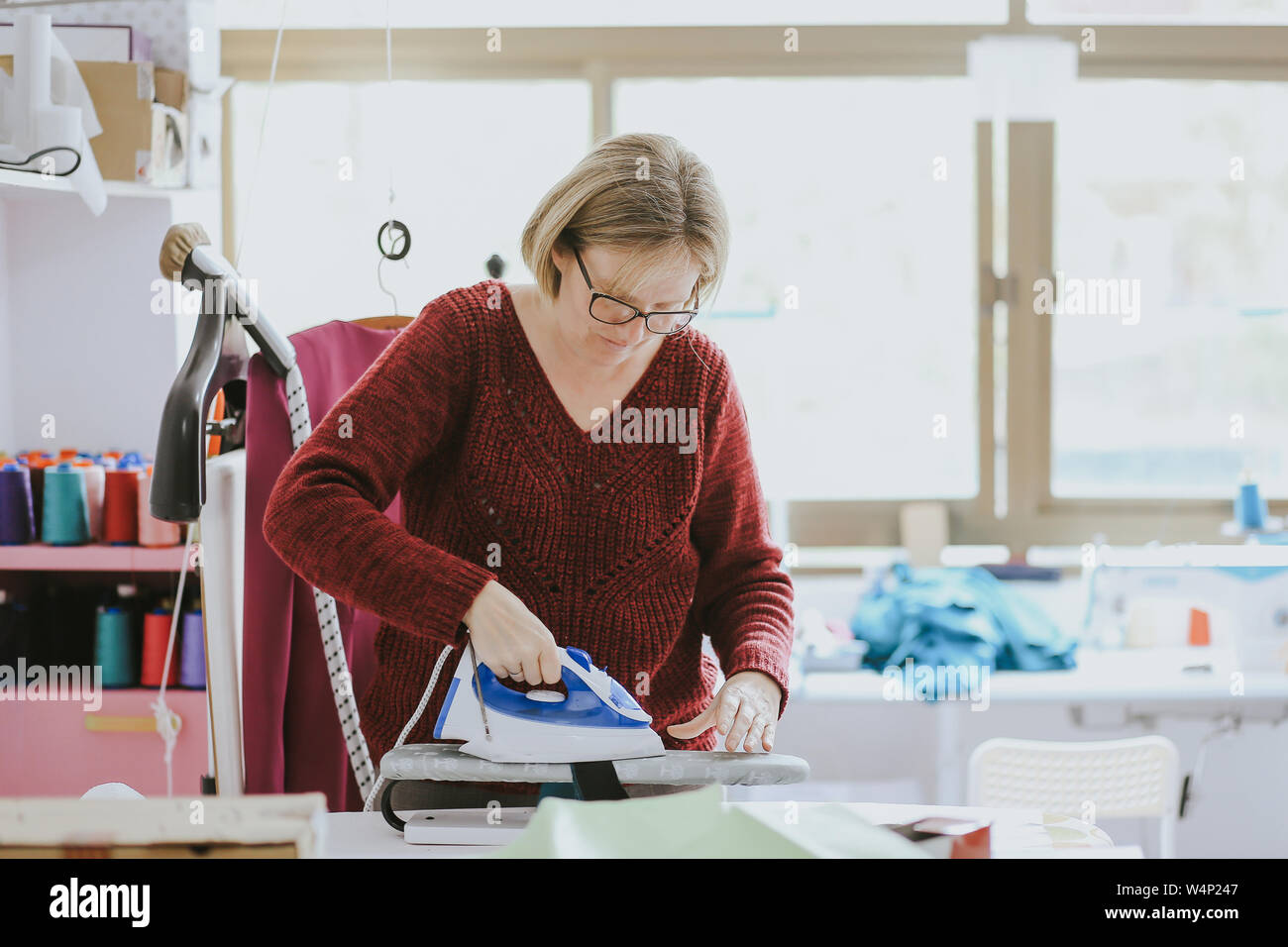 older woman with glasses ironing in a fashion design studio Stock Photo