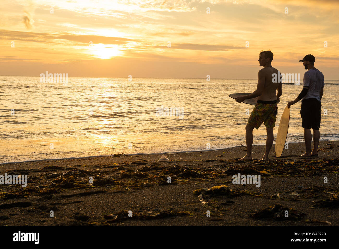 Aberystwyth, Wales, UK. 24th July 2019.  Young men skim-boarding on the waves as they break on the beach in Aberystwyth at sunset on yet another scorching  day as a plume of hot air continues to drift in from the continent. Temperatures are expected to reach the high 30’s Celsius in parts if the south east of the UK on Thursday 25 July. Photo credit Keith Morris / Alamy Live News Stock Photo