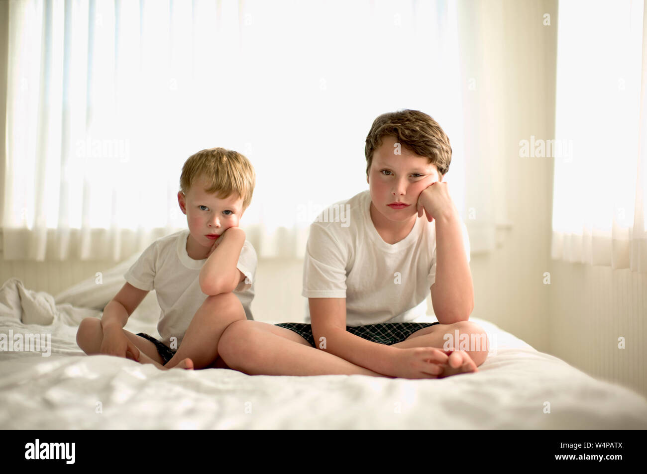 Two sulking boys sitting on a bed Stock Photo - Alamy