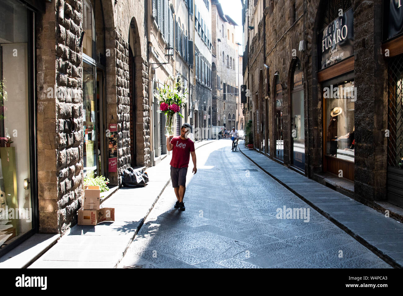 Man carries a vase filled with flesh flowers through a street in Florence, Italy Stock Photo