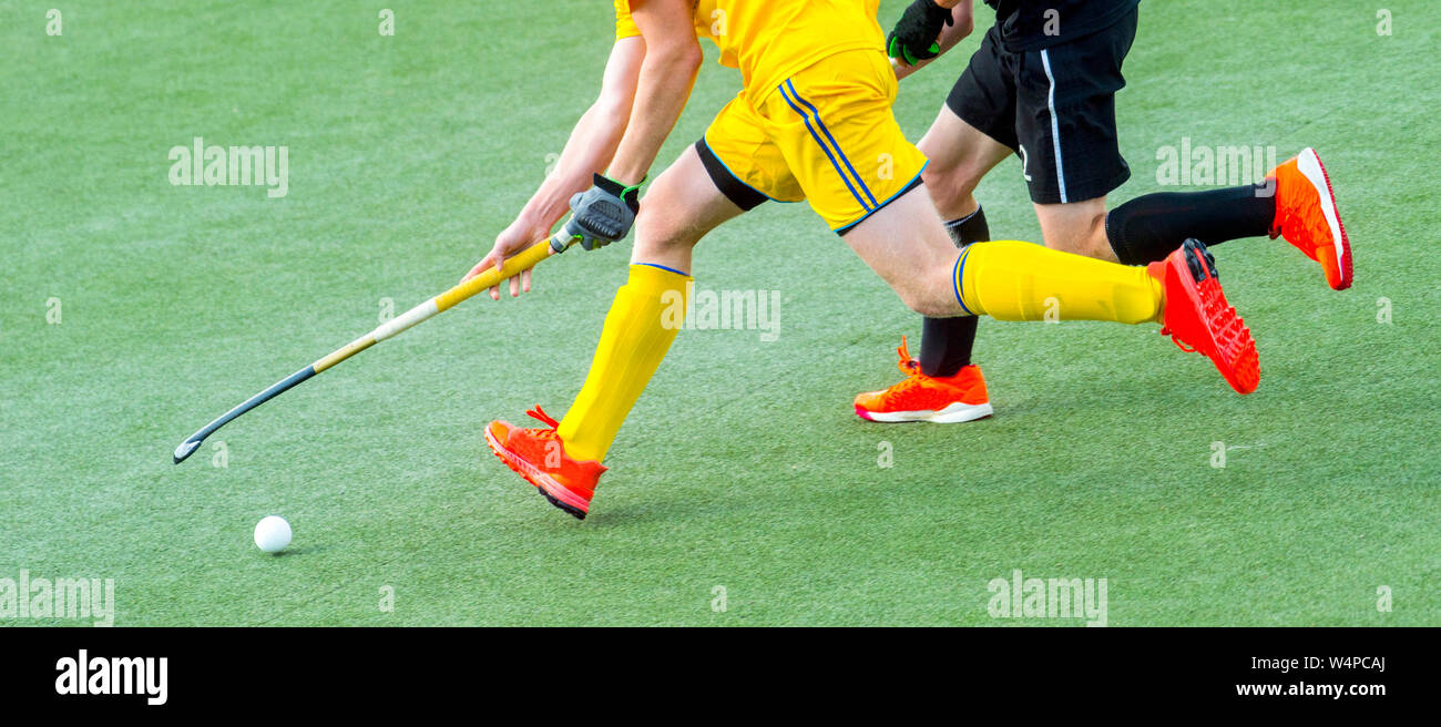 Two field hockey player, fighting for the ball on the midfield during