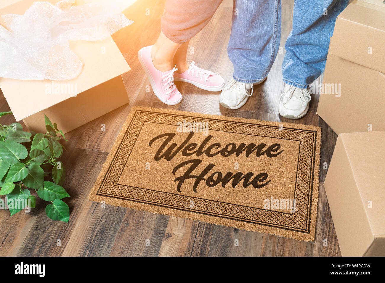 Man and Woman Unpacking Near Welcome Home Welcome Mat, Moving Boxes and Plant. Stock Photo