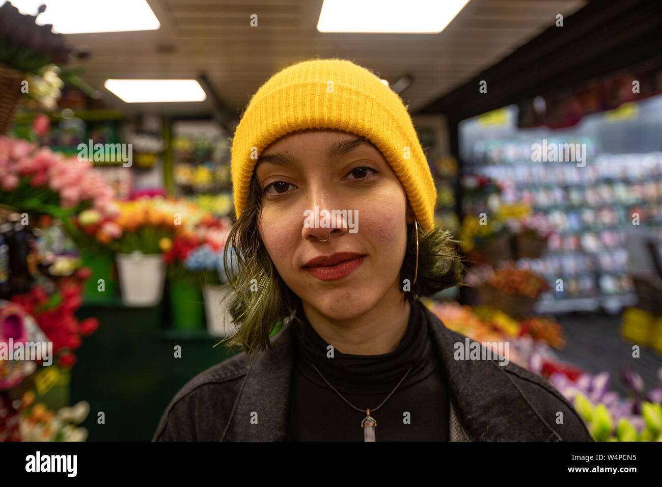 Portrait of young woman in yellow hat standing in florist. Stock Photo