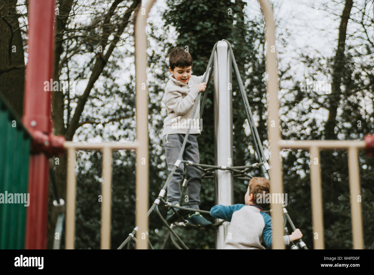 Two boys playing on climbing frame at playground Stock Photo