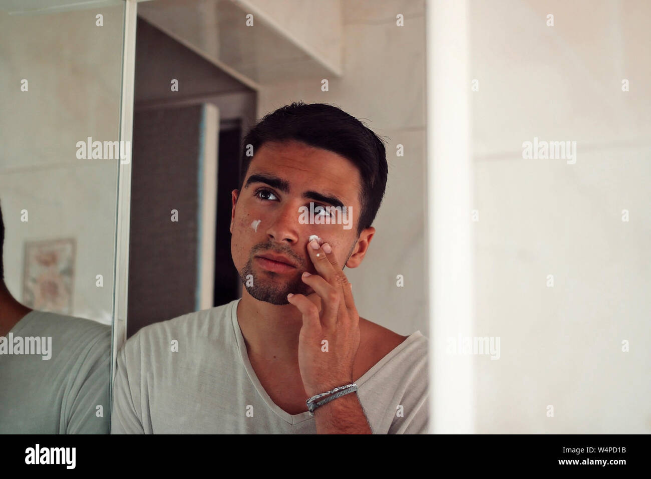 Man dressed in white putting cream on his face. Stock Photo