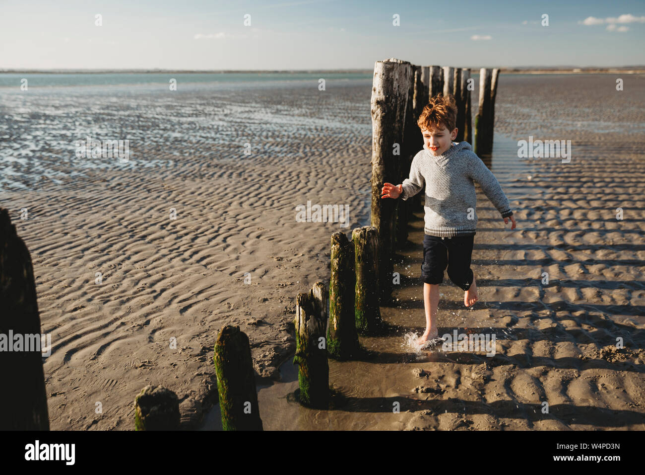 Boy running through water at beach against decaying breakwater pilings Stock Photo