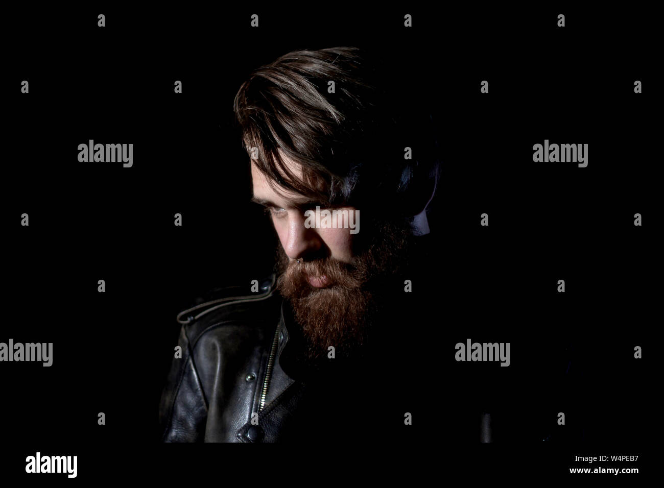 brooding bearded hipster in a leather jacket looking somewhere to the side. isolated on black background Stock Photo
