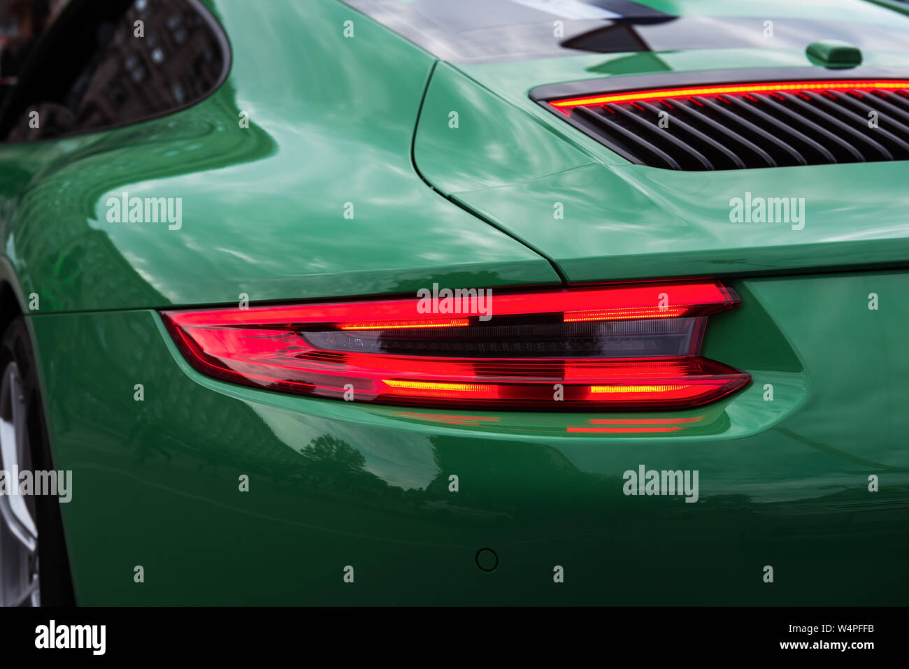 Green sports car with red backlight on. Closeup of a luxury car body. Modern LED light. Rear light strip. Stock Photo