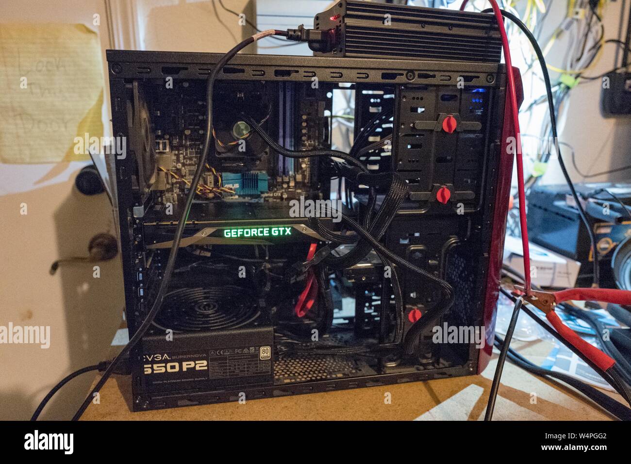 Computer equipped with glowing NVidia 1070 graphics card, with case open,  on a workbench connected to a maze of wires while undergoing testing, while  being configured for cryptocurrency mining of Bitcoin and