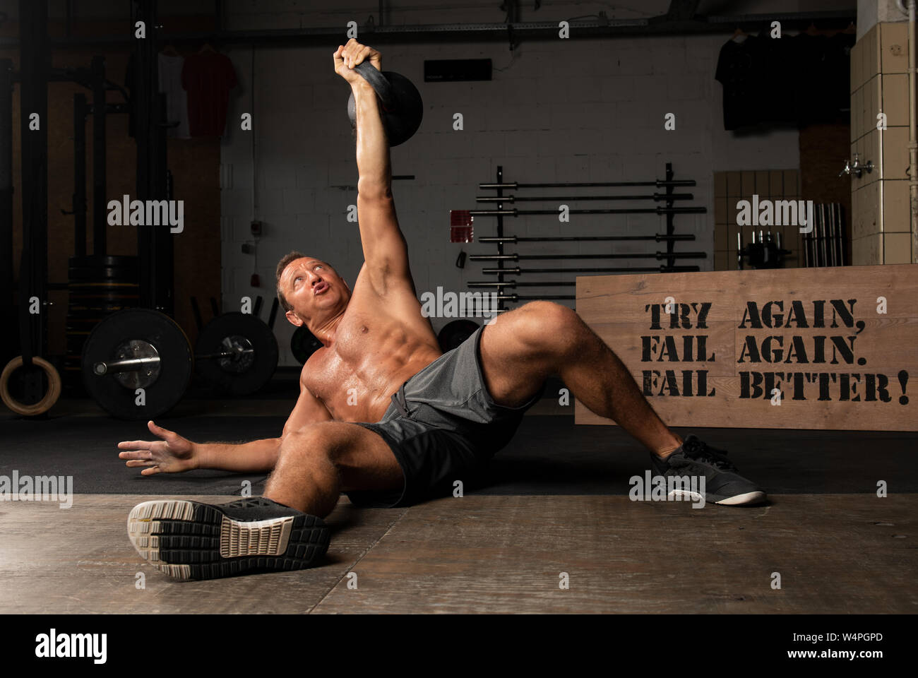 An athletic suntanned man with strong abs is doing weight lifting with a kettlebell in a gym. Exercise Turkish get up. Stock Photo