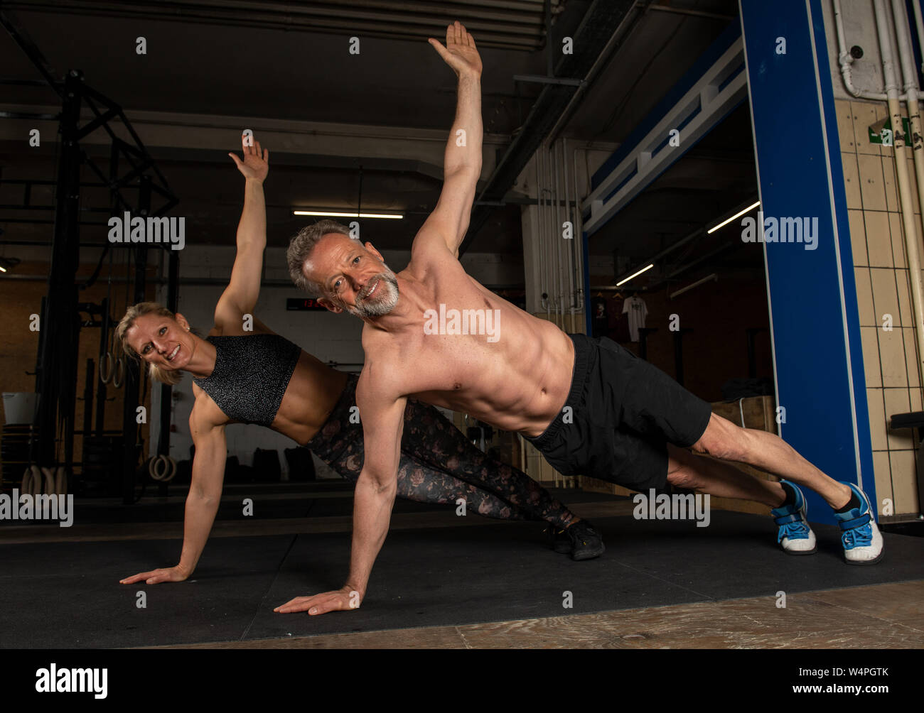 A middle aged attractive and athletic couple is doing a partner workout together in a gym.Strong man and woman are laughing and doing t-push ups. Stock Photo