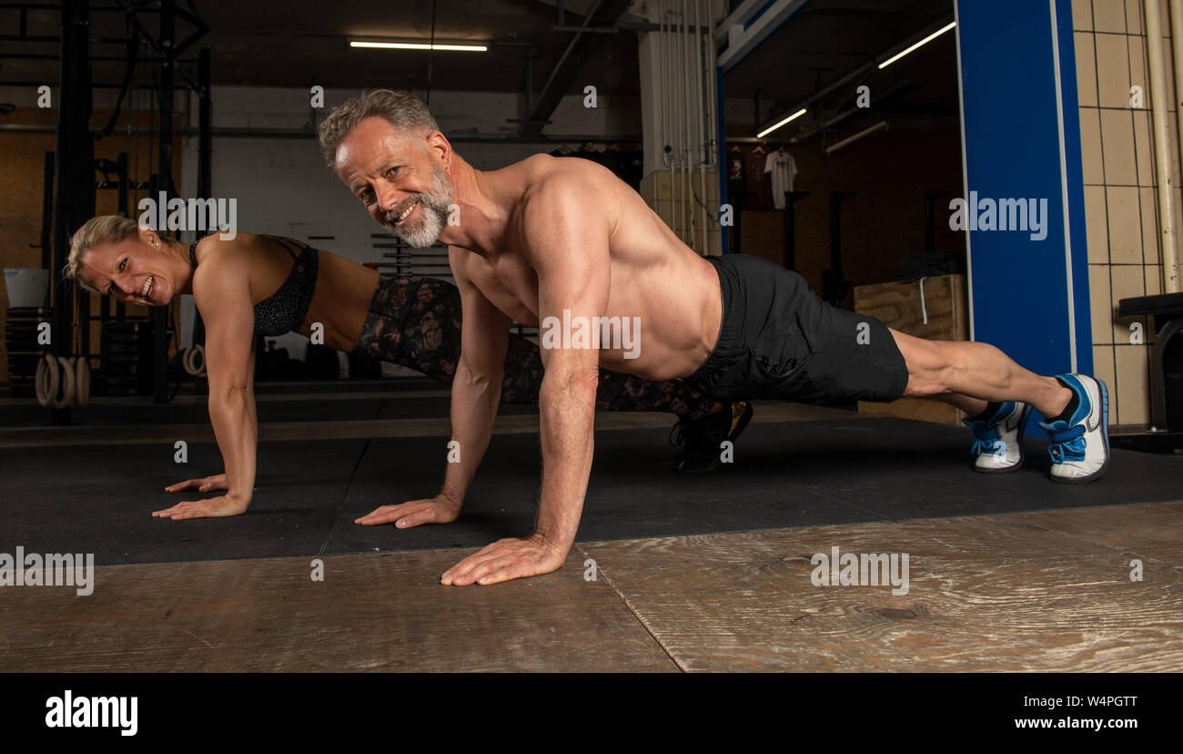 A middle aged attractive and athletic couple is doing a functional fitness training together. Strong man and woman are laughing in gym. Doing Pushups. Stock Photo