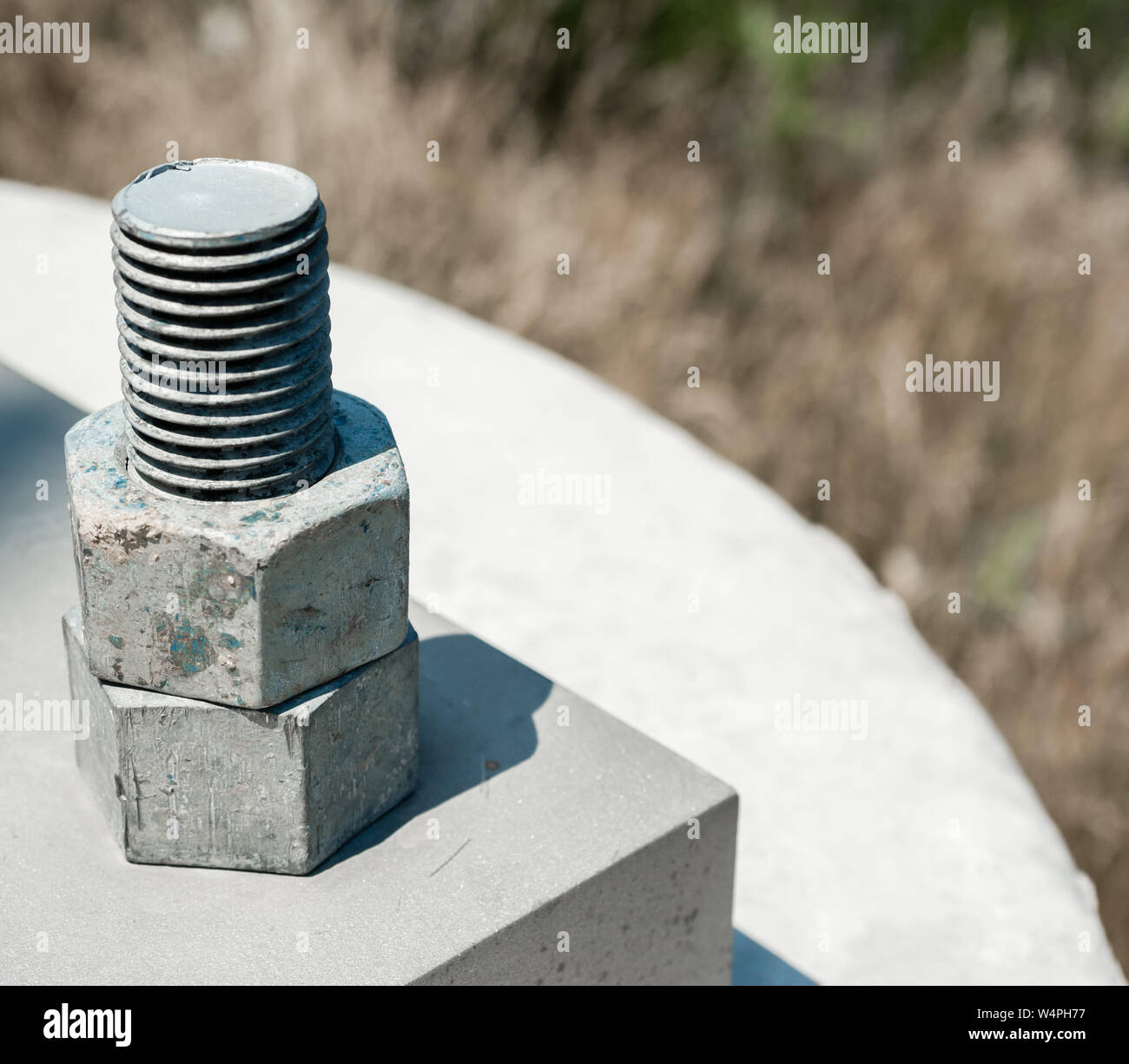 Two hexagonal steel nuts threaded on bolt attached to concrete block. Stock Photo