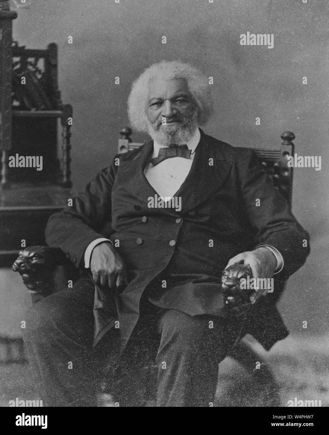 Black and white portrait photograph of African-American abolitionist, writer, orator, statesman, and social reformer, Frederick Douglass, depicted seated, in three-quarter length view, wearing a dark, double-breasted suit with a bow tie, facing the camera, with white hair and beard, and a serious expression on his face, 1880. From the New York Public Library. () Stock Photo
