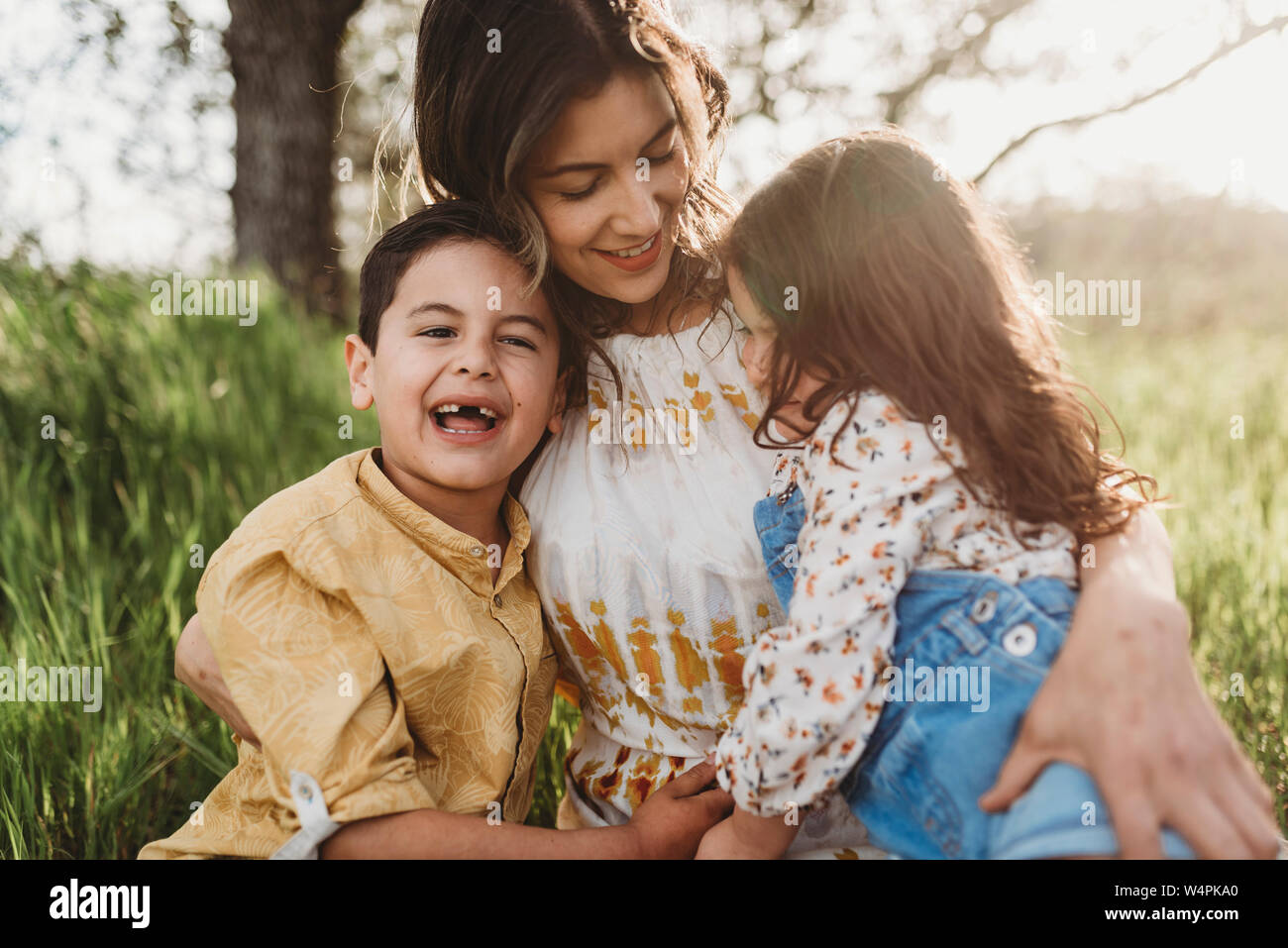 Mother, son, and daughter cuddling on blanket in backlit field Stock