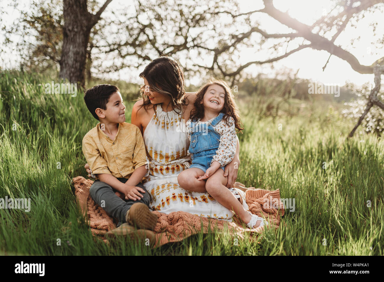 Mother, son, and daughter in backlit field smiling at each other Stock Photo