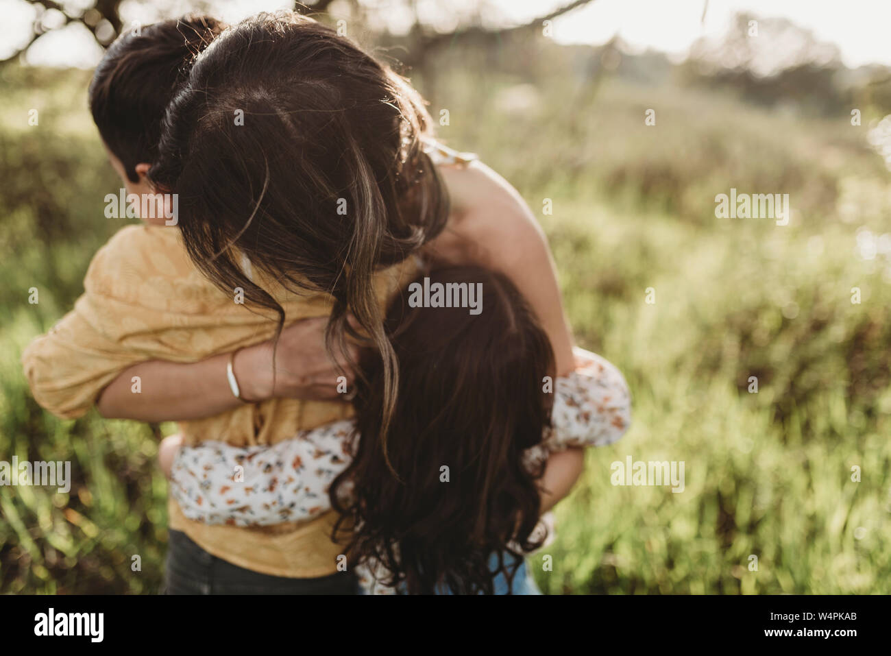 Close up view of mother, daughter and son hugging in backlit field Stock Photo