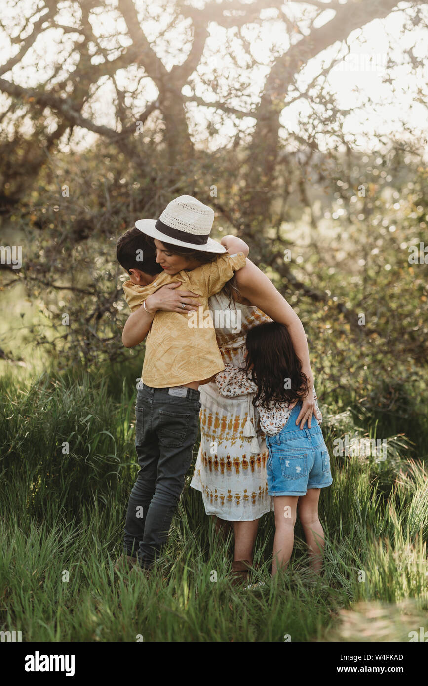 Full length view of mother hugging son and daughter in backlit field Stock Photo