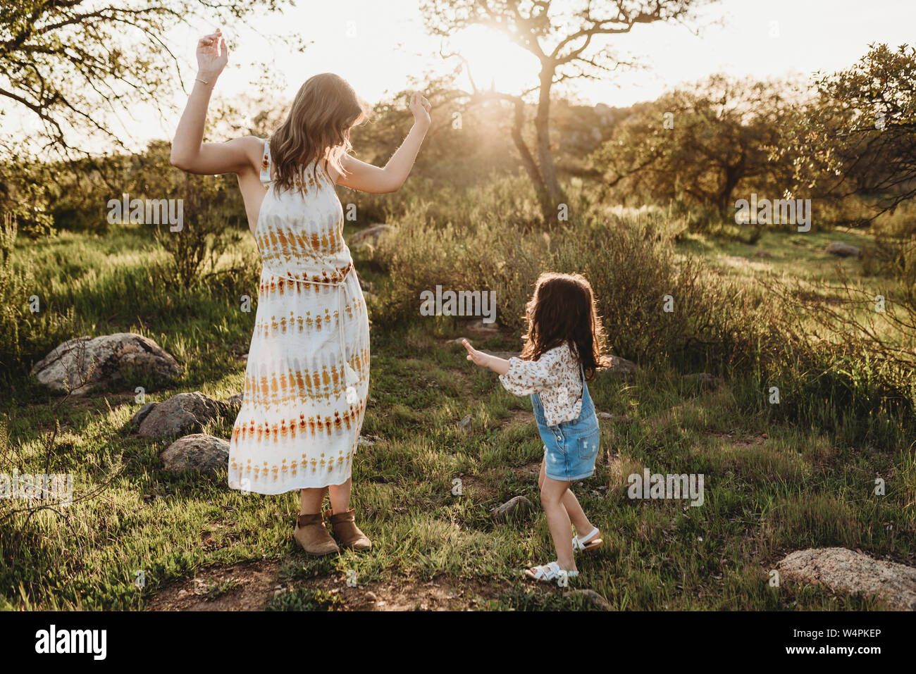 Young mother and daughter dancing in sunlight in bright field Stock Photo