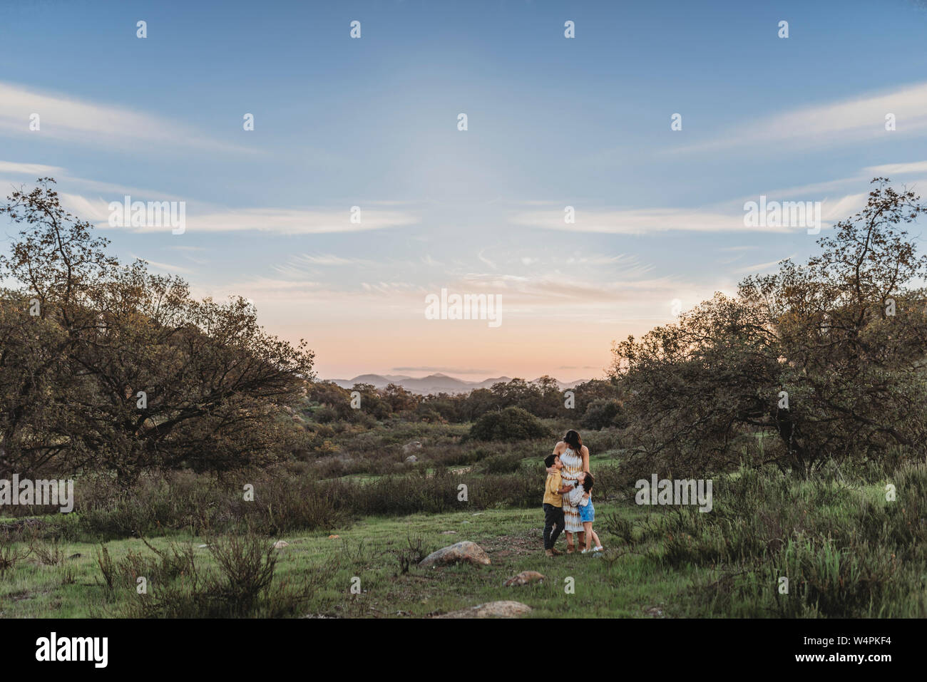Landscape of young mother and children hugging under blue sky in field Stock Photo