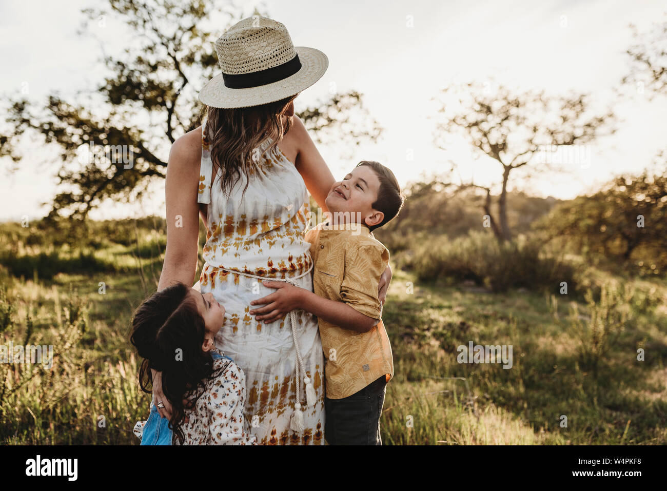 Front view of youthful mom and young children hugging in field Stock Photo