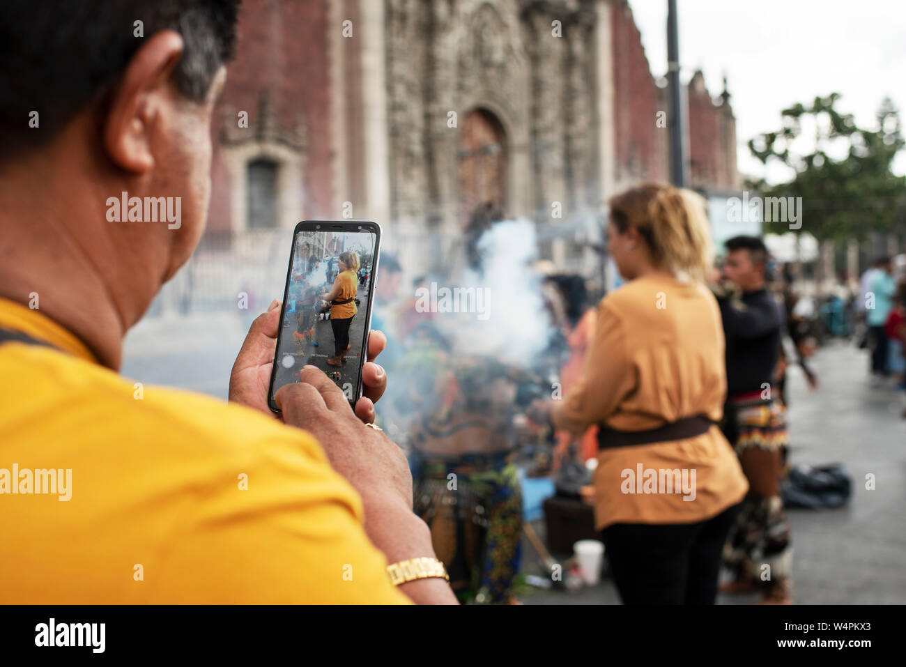 Mexican woman receiving copal spiritual 'cleansing' ritual at the Zocalo while her man recording it on his phone. Mexico City, CDMX, Mexico, Jun 2019 Stock Photo
