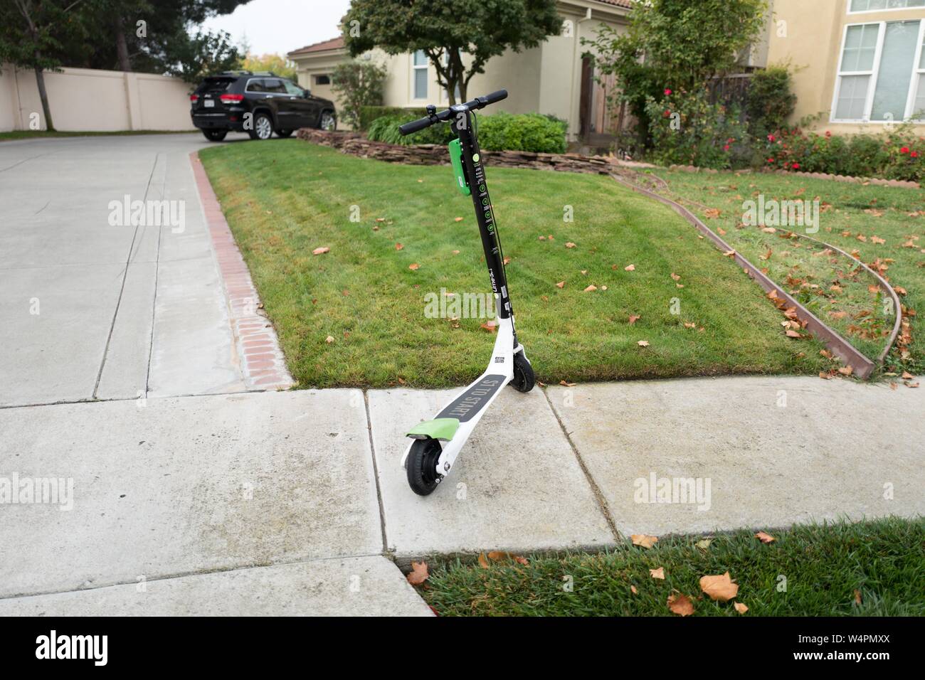 Lime scooter from sharing economy startup Lime, parked on a sidewalk in front of a suburban home