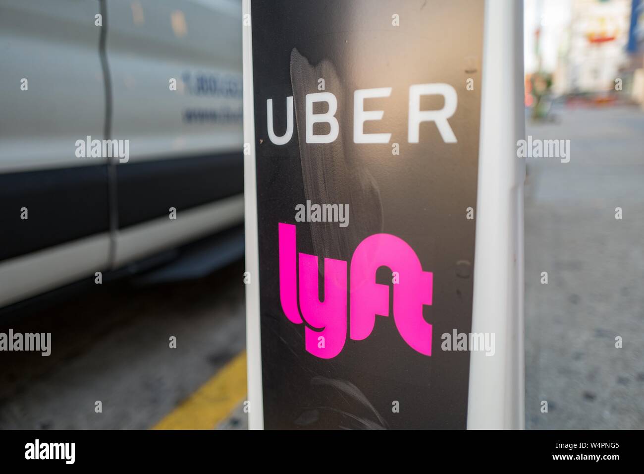 Close-up of vertical sign with logos for ridesharing companies Uber and Lyft, with wheels of a car in the background, indicating a location where rideshare pickups are available in downtown Los Angeles, California, October 24, 2018. () Stock Photo