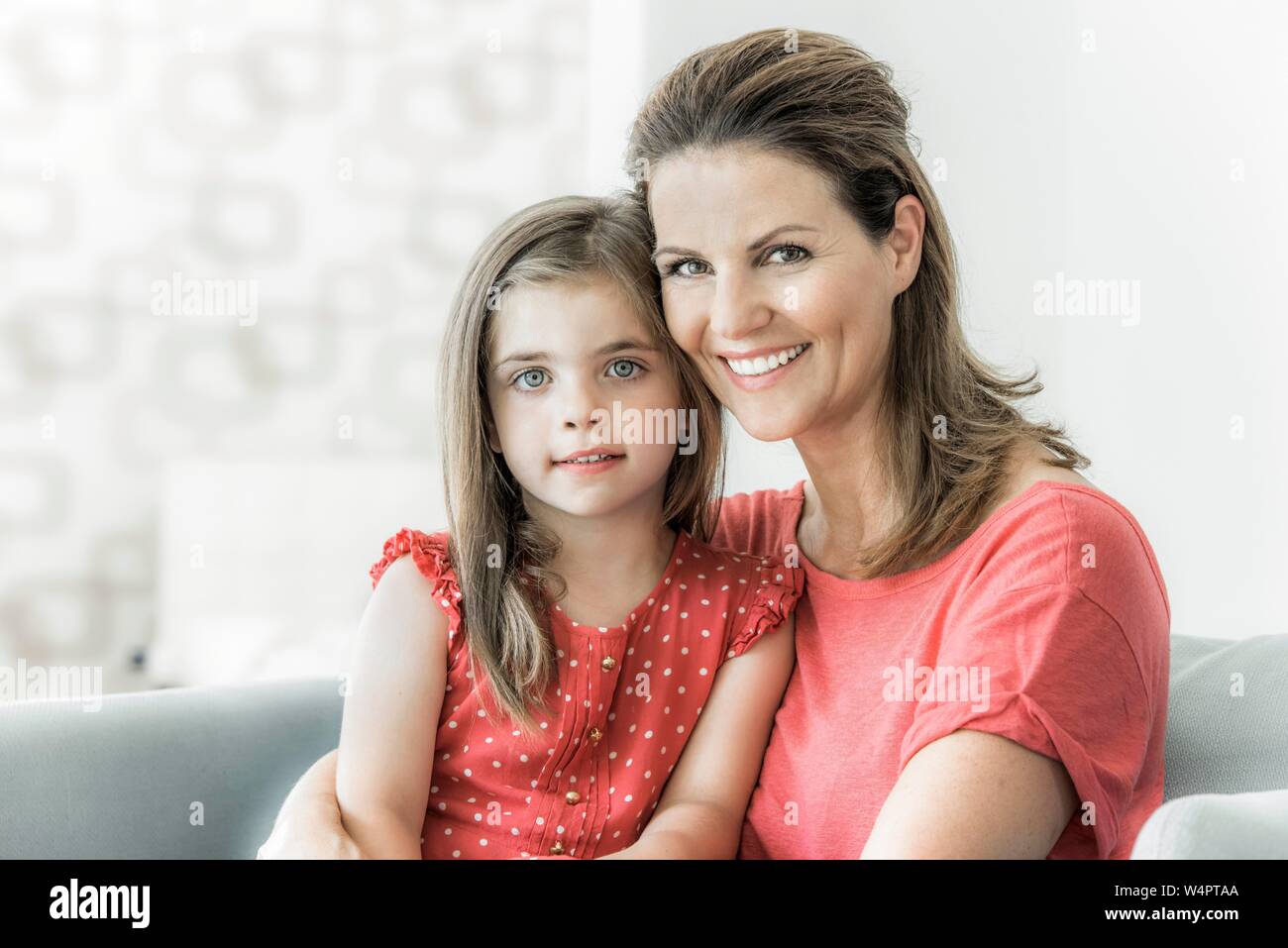 Mother and daughter sit together on the couch and look into the camera