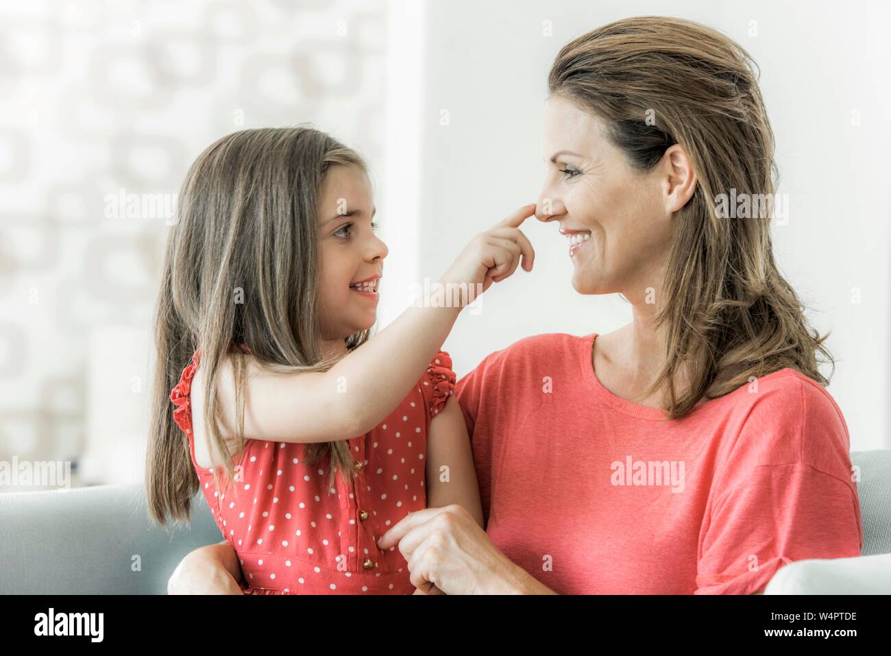 Mother and daughter sit on the couch together and look at each other, daughter grabs mother's nose, smile, Germany Stock Photo
