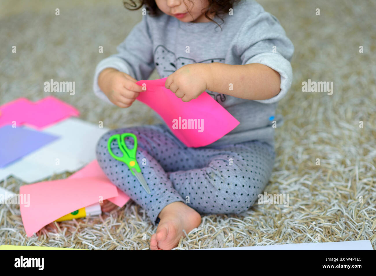 A three-year-old toddler girl cuts out with a scissors, craft with kids, cut, hobby, free time Stock Photo