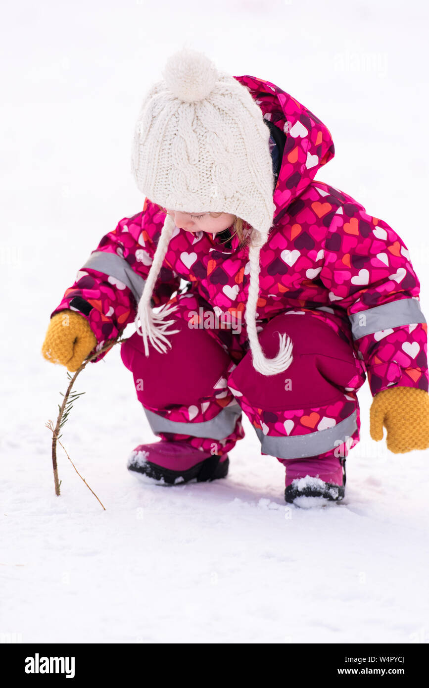 happy cute little girl wearing a red snow suit and white hat while having fun and playing on