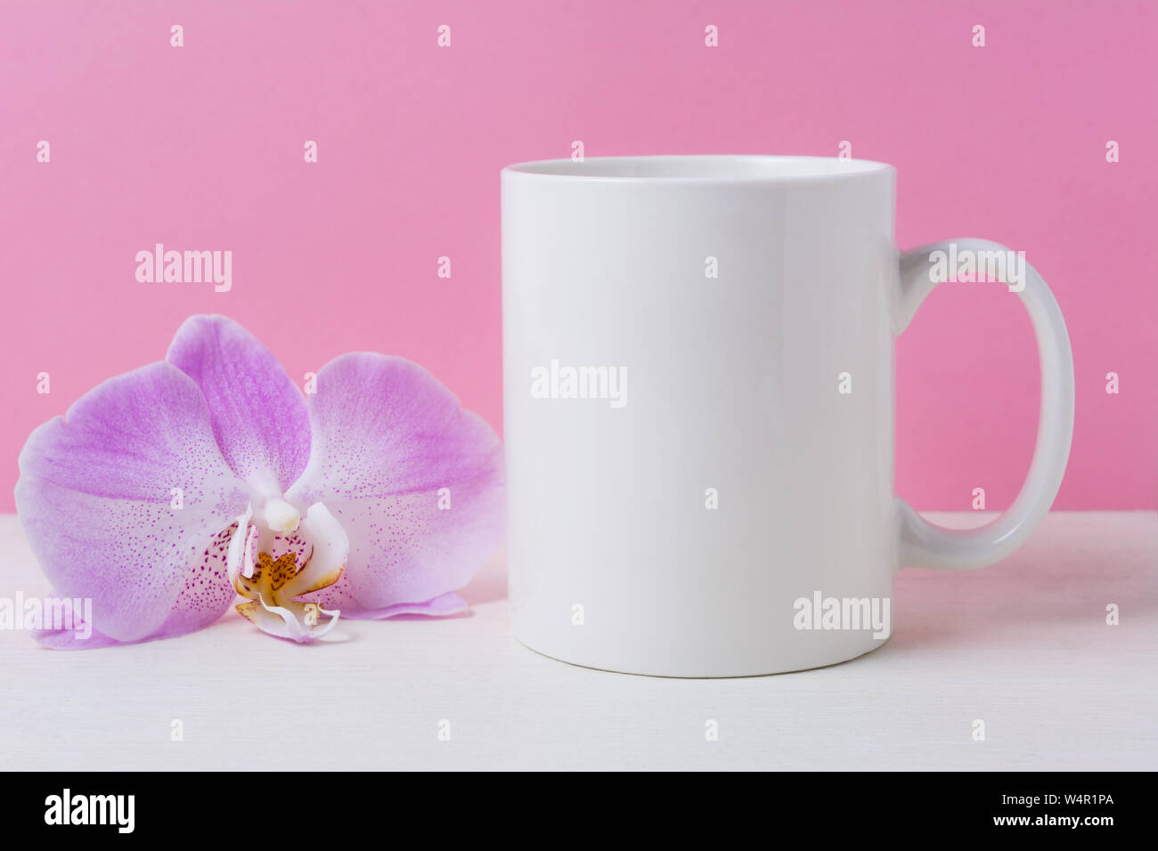 White coffee mug mockup on the pink background with purple orchid. Empty mug mock up for design promotion. Stock Photo