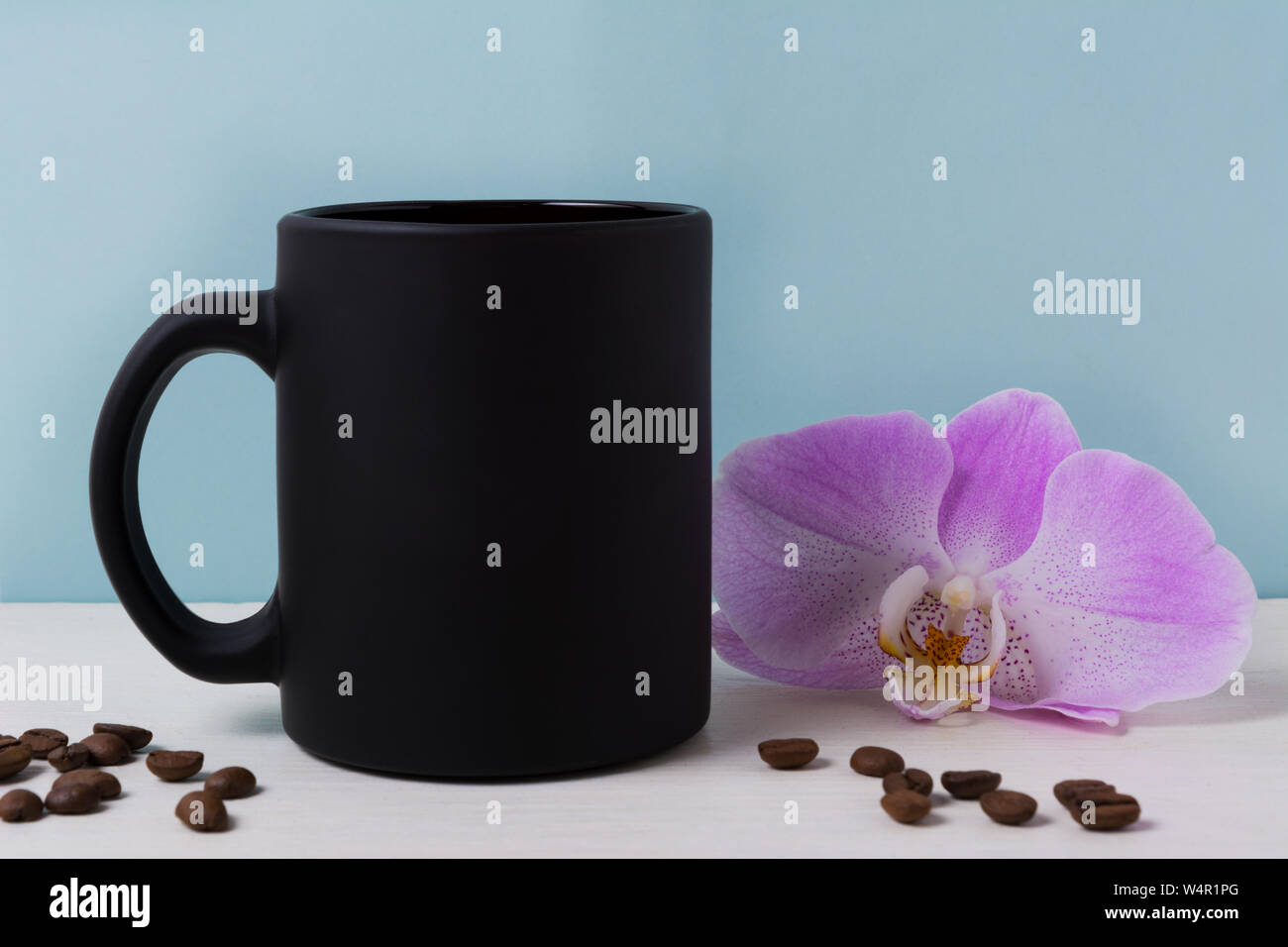Black coffee mug mockup with purple orchid and coffee beans. Empty mug mock up for brand promotion. Stock Photo