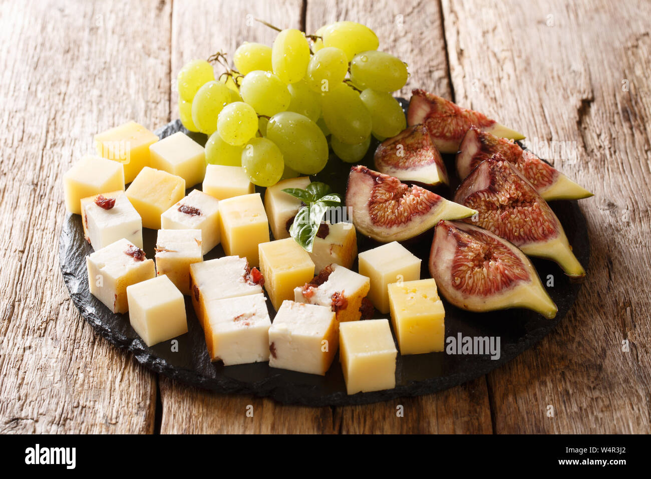 Gourmet antipasti appetizer of various cheese, fresh grapes and figs close-up on a slate board on the table. horizontal Stock Photo