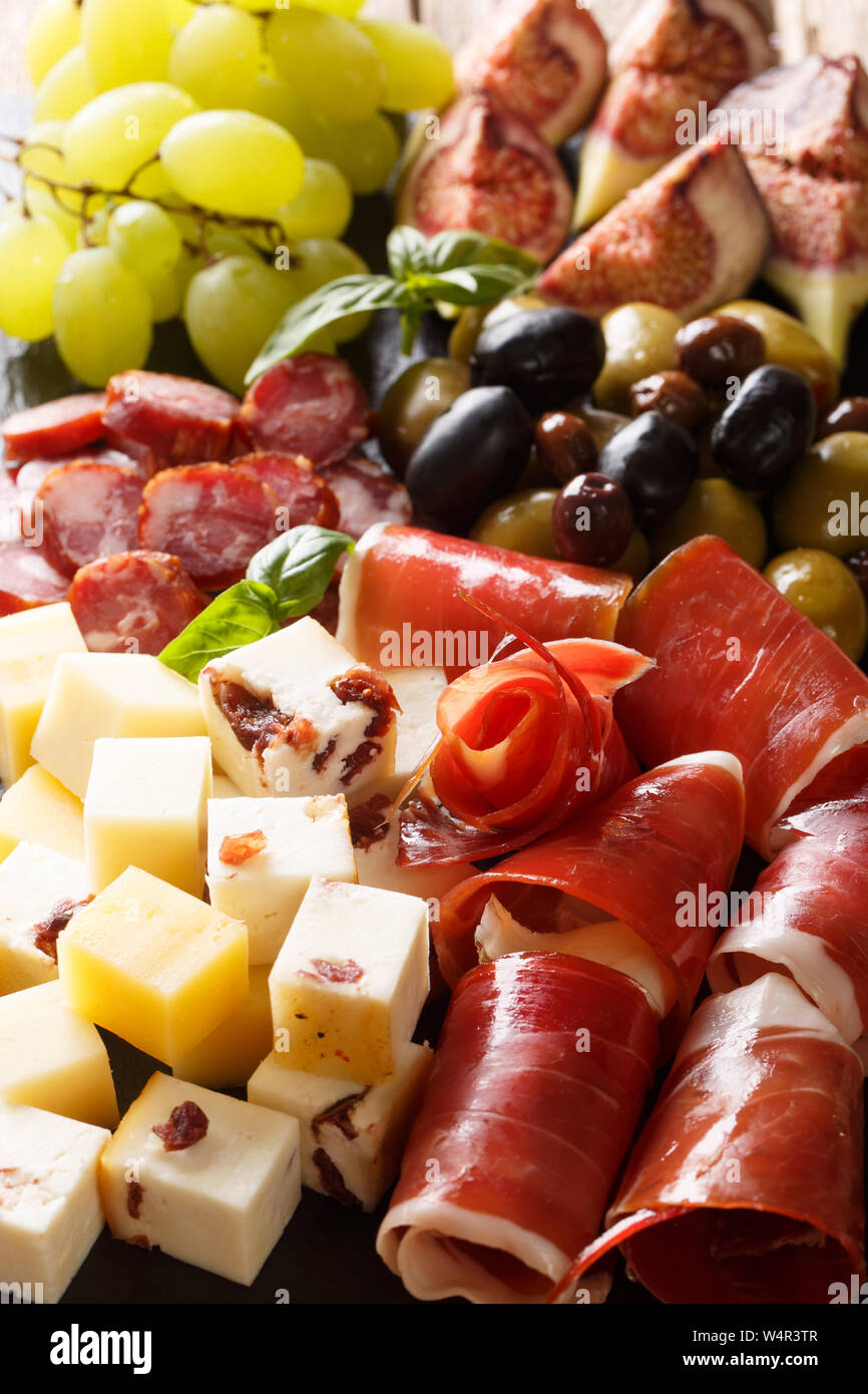 Antipasti appetizer of cheese platter, prosciutto ham, grapes, figs, sausages and olives close-up. Vertical background Stock Photo