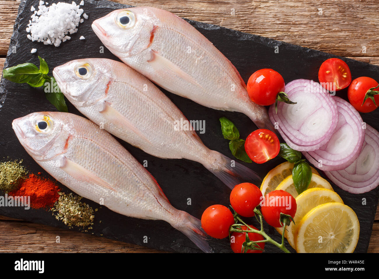 Raw pink dorado or gilt-head sea bream fish with spices, vegetables and lemon close-up on a slate board on a table. horizontal top view from above Stock Photo