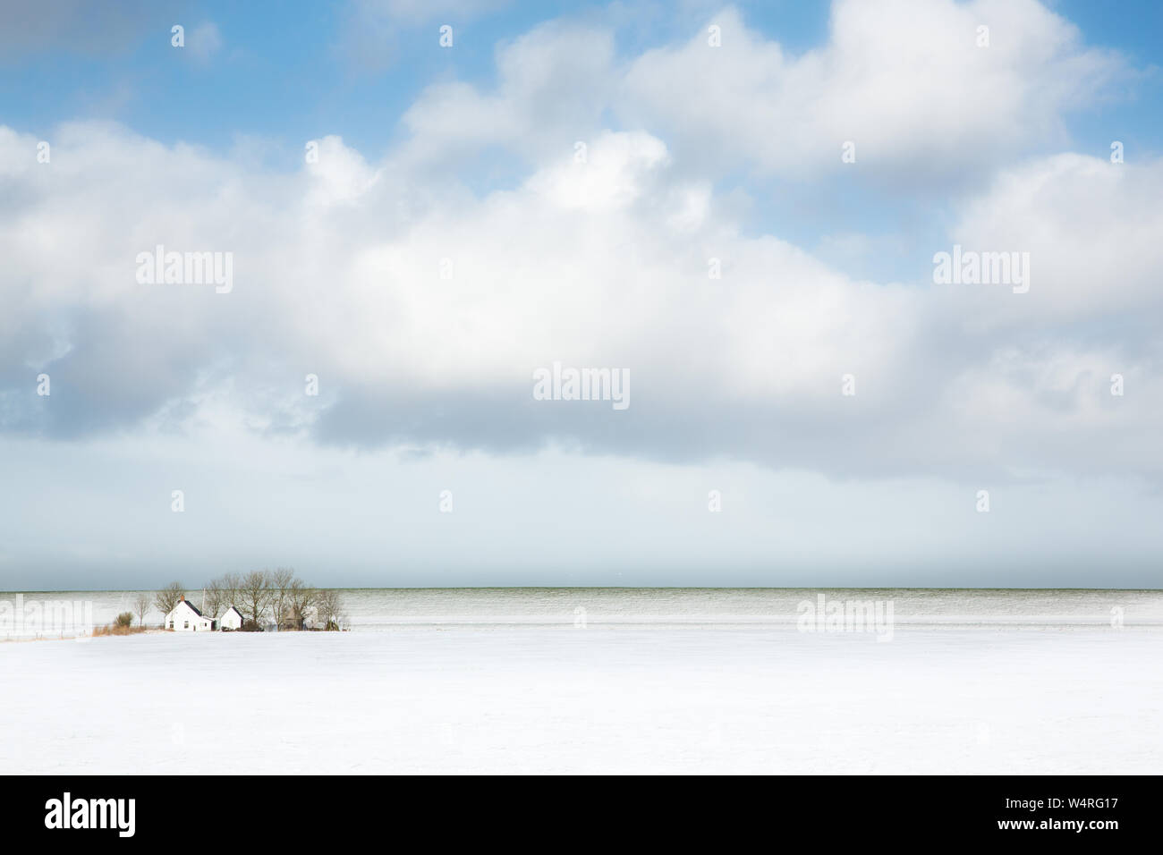 Winter landscape with snow in the fields and a lone farm in the background and a big sky - The Netherlands Stock Photo