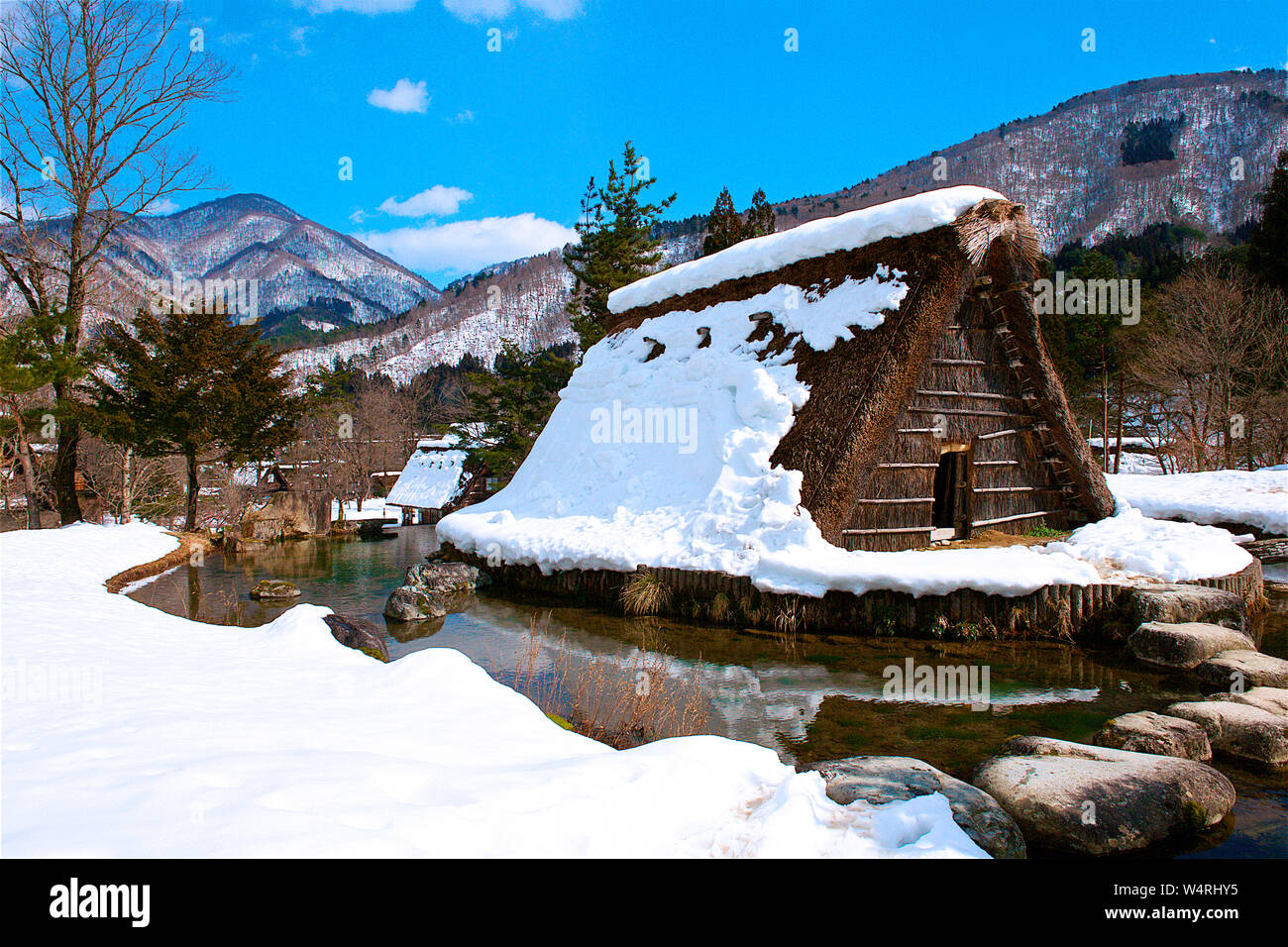 Wooden village shelter with straw roof surrounded by water with mountain on horizon in winter, Shirakawa village, Ono District Stock Photo