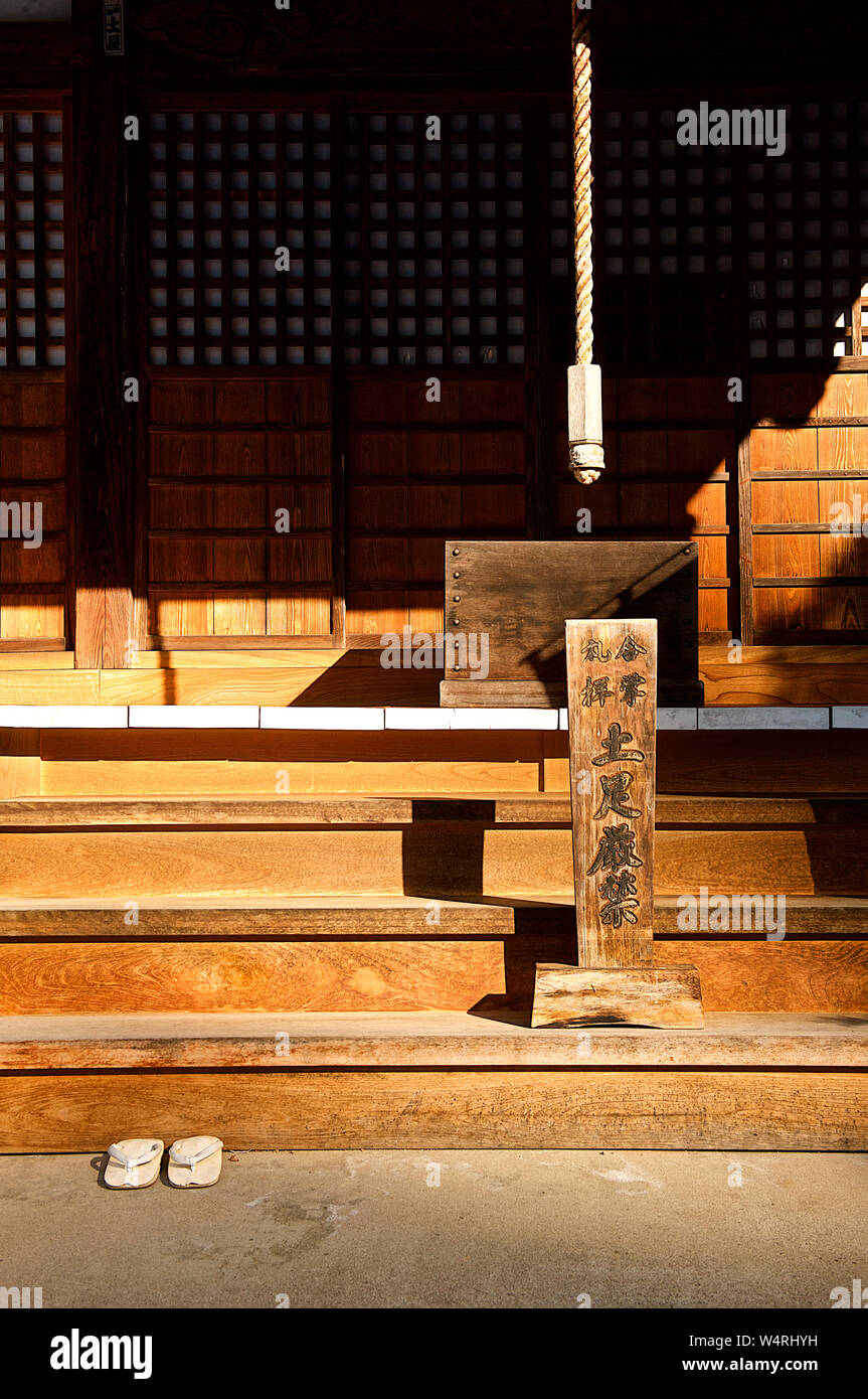 Sunlit wooden entrance steps to temple with white thongs left below, Hida-Takayama, Takayama, Gifu Prefecture, Japan Stock Photo