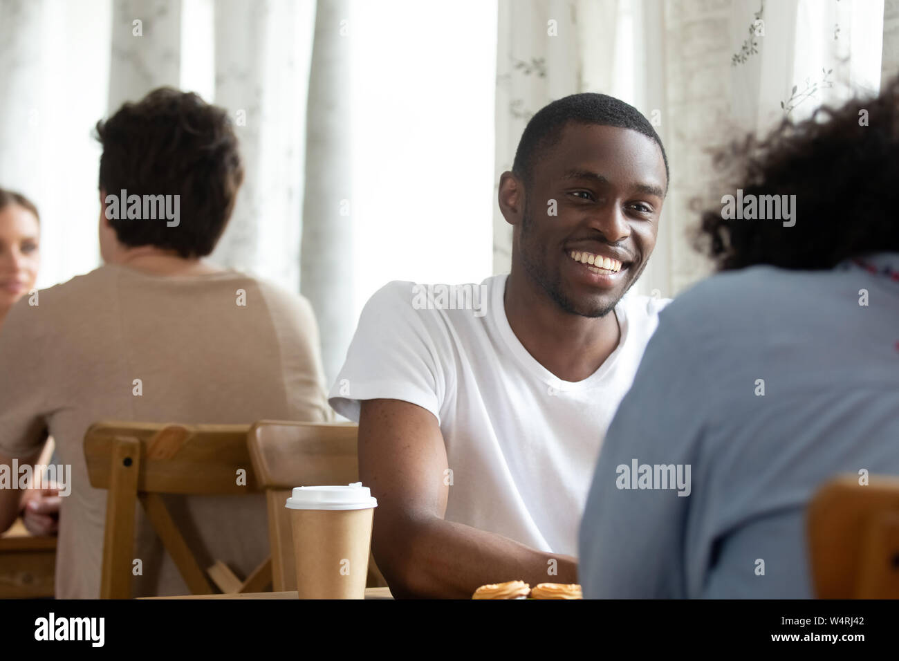 Happy smiling black guy sitting in coffeehouse with friend Stock Photo