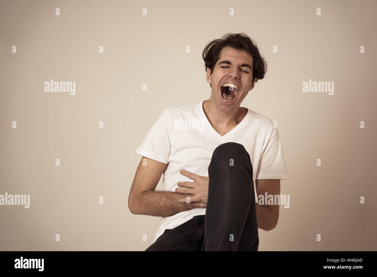 Portrait of young millennial funny male having fun bursting into laughing loudly after hearing humor anecdotes and jokes. Isolated against neutral bac Stock Photo