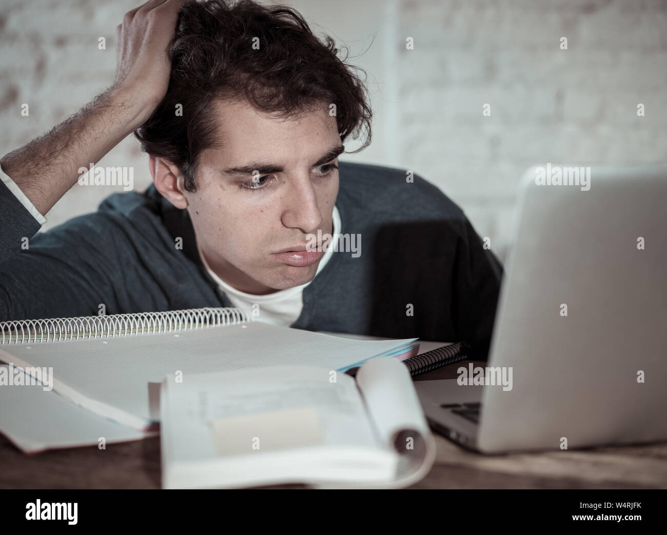 Overworked and tired male student working late at night on laptop trying not to fall asleep feeling fatigued, worried and sad. Moody dark light. Final Stock Photo