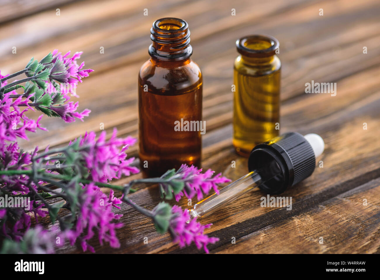 bottles with essential oils, dropper and heather plant on wooden