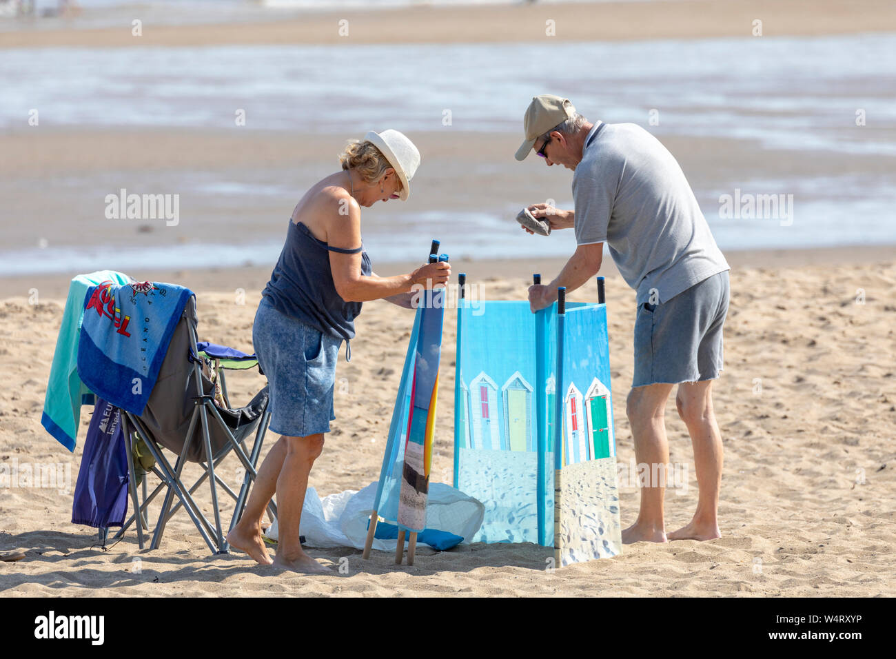 Couple hammering in stakes for a wind breaker and shade breaker on Colwyn Bay Beach, North Wales during heatwave weather in the area of Wales Stock Photo
