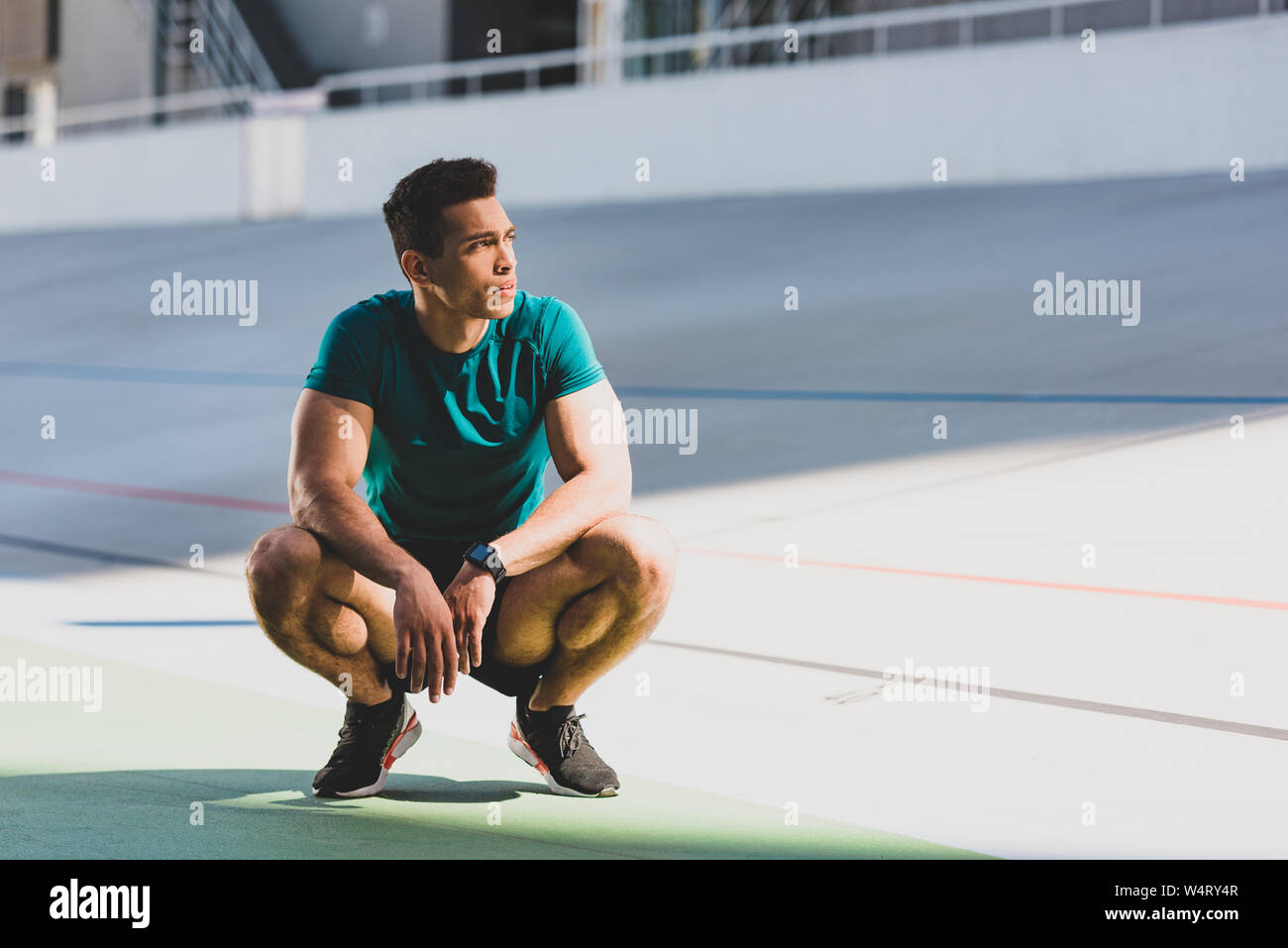 front view of mixed race sportsman squatting and looking away at ...